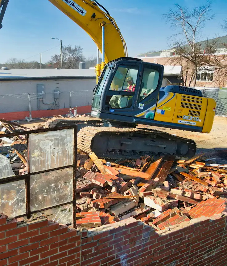 Heavy machinery breaking up a structure and loading demolition debris for hauling