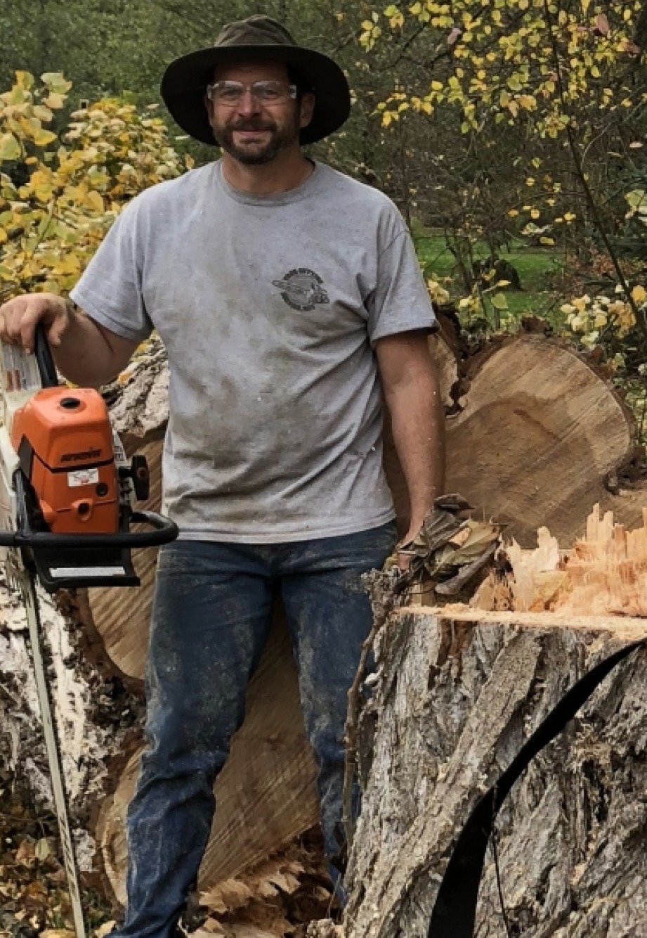 Bob standing with a chainsaw beside the trunk of a large tree he has just felled
